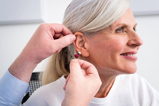 Ältere Frau erhält ein modernes Hörgerät zur Verbesserung des Hörvermögens angepasst.